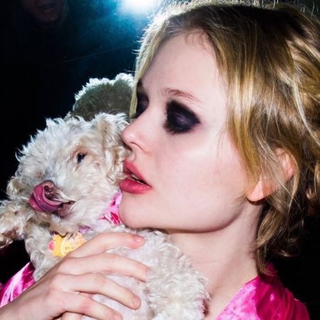 Emily Alyn Lind in a pink top hugs her puppy. 
